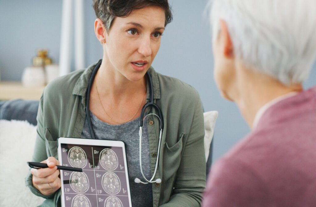 Female doctor with stethoscope around neck points to tablet with brain scans in front of older woman who is blurred in the foreground.