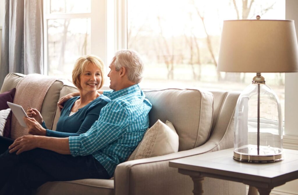 A senior couple cuddles on the couch of their assisted living apartment, enjoying spending quality time together