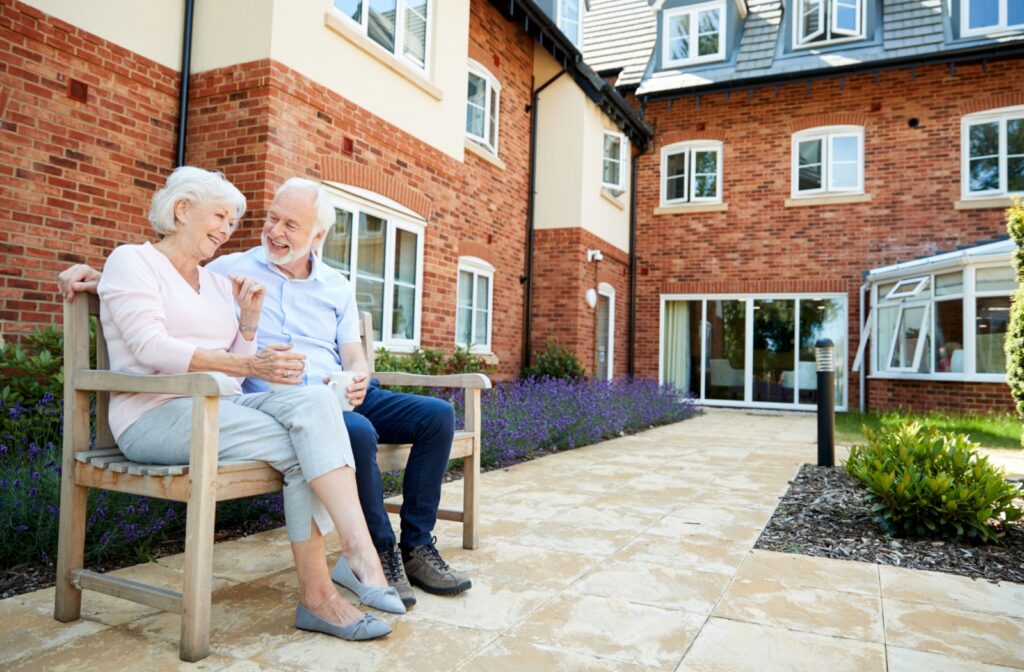 A senior couple sits on a bench outside in the courtyard of their assisted living community.