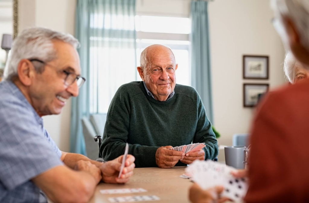 A senior is playing cards with friends while smiling in an assisted living community.
