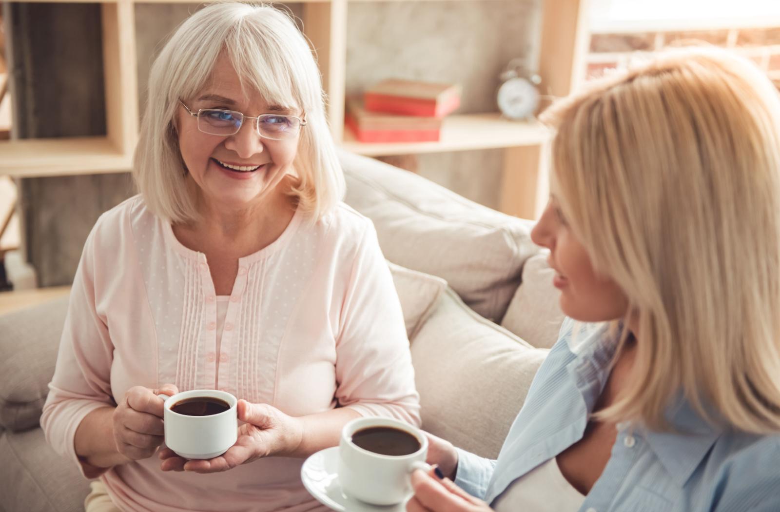 An adult child and their senior parent reminisce over a cup of coffee.
