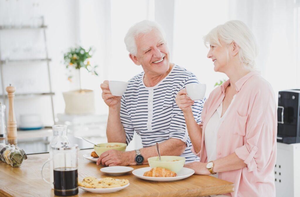 A senior couple smile at each other while drinking coffee and eating breakfast